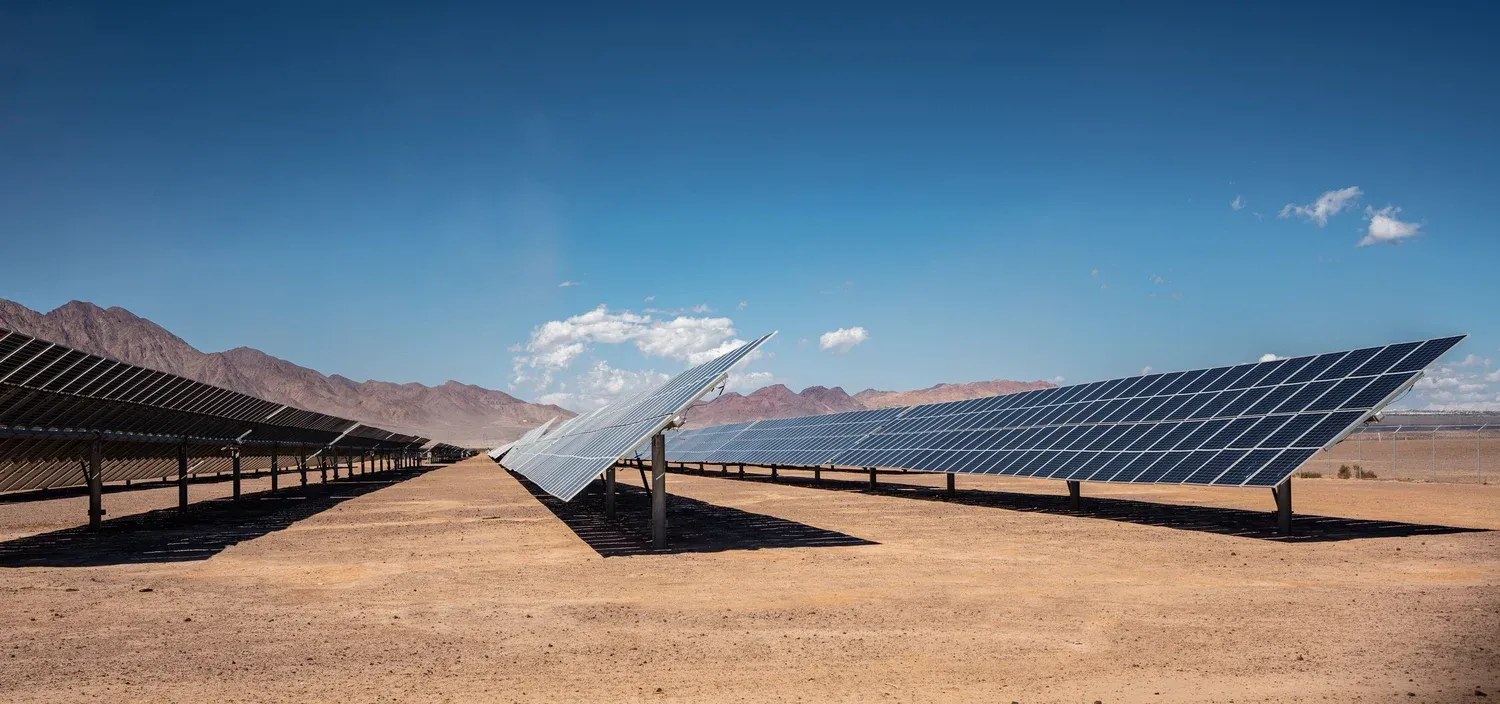 Panneaux solaires dans un paysage désertique, avec des montagnes à l’arrière-plan sous un ciel bleu.