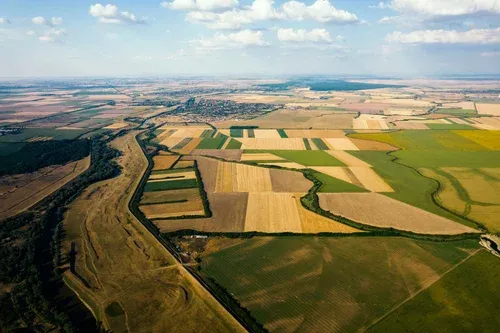 Vue aérienne de terres agricoles en damier, traversées par une rivière, avec un village au loin.